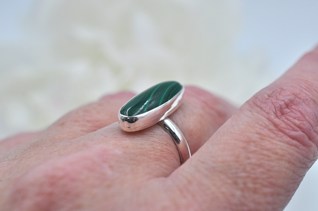 Silver ring with a green stone on a finger against a blurred background