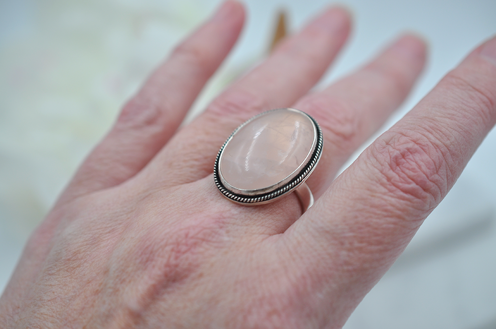 Hand wearing a ring with a pink stone on a blurred background