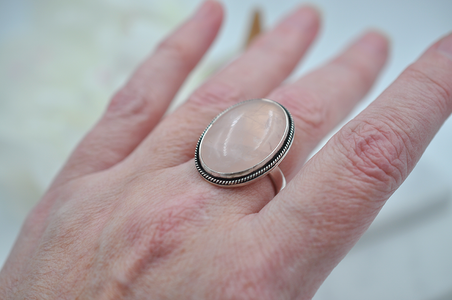 Hand wearing a ring with a pink stone on a blurred background