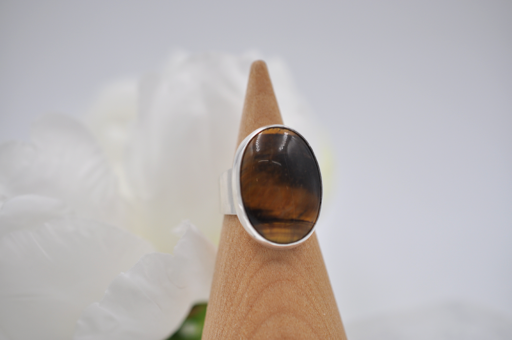 Silver ring with a brown tiger's eye stone on a wooden ring cone against a white background