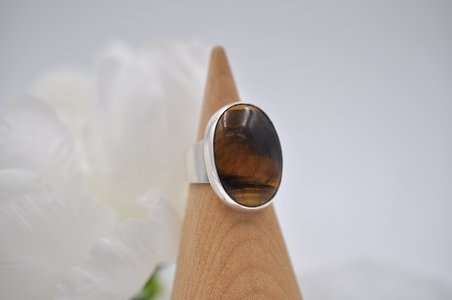 Silver ring with a tiger's eye stone on a wooden stand with a white flower background