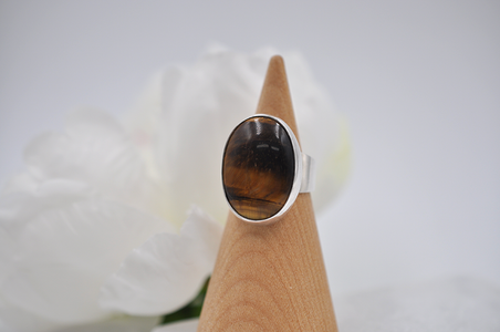 Silver ring with a dark brown tiger's eye stone on a wooden stand against a white background