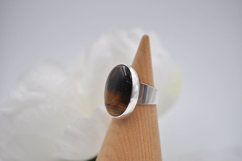 Silver ring with a dark brown tiger's eye stone showing the tapered ring band on a wooden stand against a white background