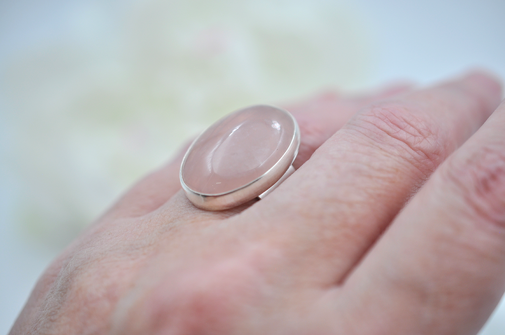 Hand wearing a ring with a pink stone on a blurred background