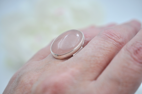 Hand wearing a ring with a pink stone on a blurred background
