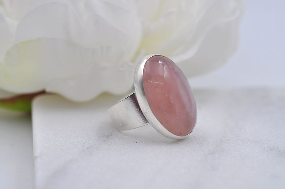Silver ring with a pink stone on a white surface with a white flower in the background