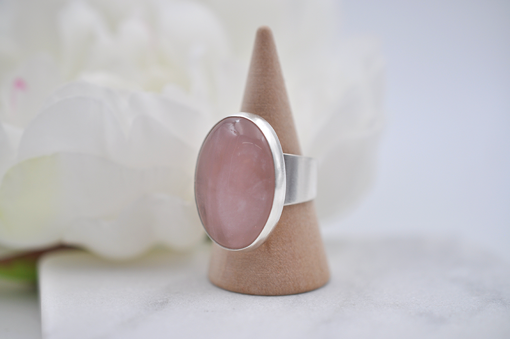 Silver ring with a pink stone on a cone-shaped stand against a white background