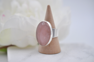 Silver ring with a pink stone on a cone-shaped stand against a white background
