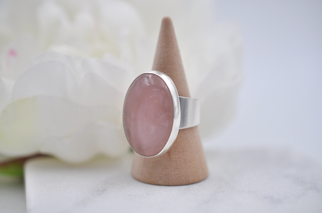 Silver ring with a pink stone on a cone-shaped stand against a white background