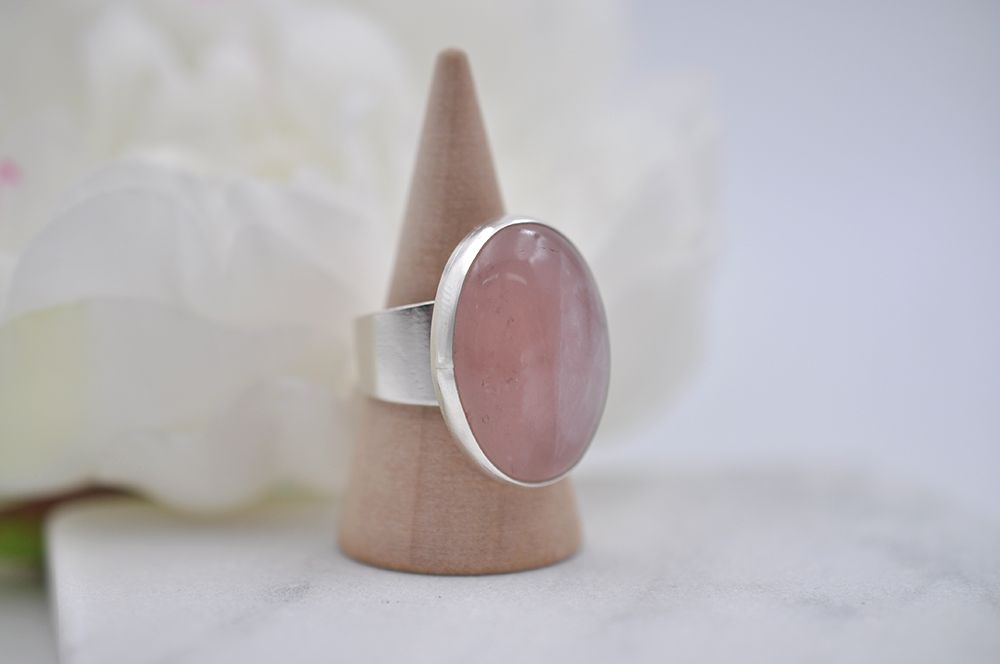 Pink stone ring on a wooden stand with a white flower background