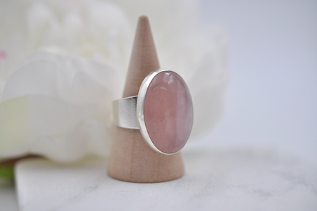 Pink stone ring on a wooden stand with a white flower background