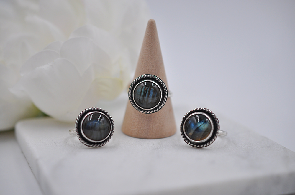 Three silver rings with multi-colored gemstones on a white surface with a beige cone.