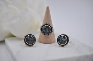 Three silver rings with multi-colored gemstones on a white surface with a beige cone.