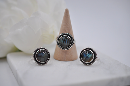 Three silver rings with multi-colored gemstones on a white surface with a beige cone.