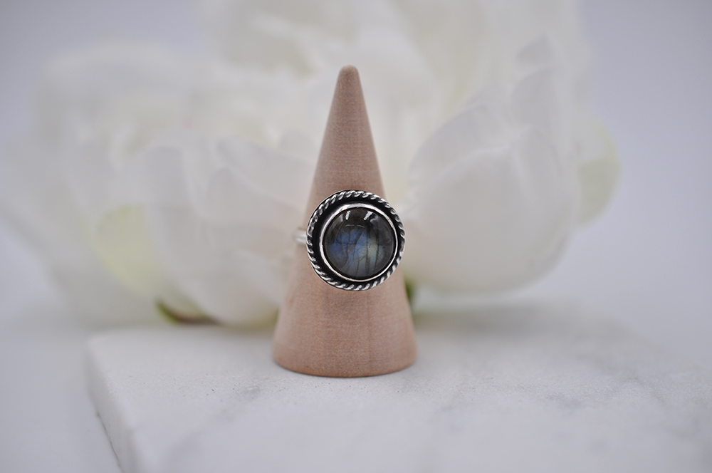 Silver ring with a round gemstone on a wooden cone against a white background