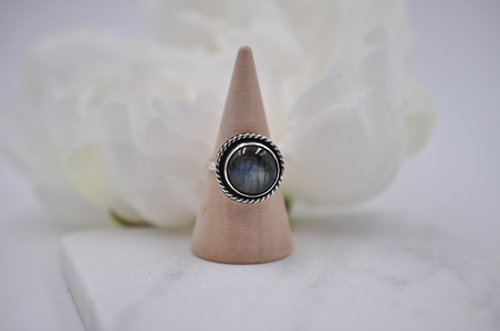 Silver ring with a round gemstone on a wooden cone against a white background