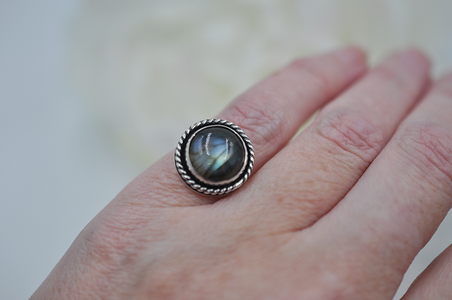 Silver ring with a round stone on a person's finger against a blurred background