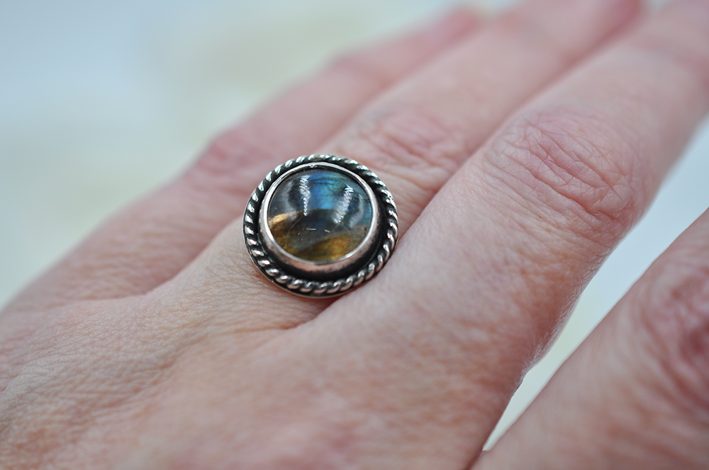 Silver ring with a gemstone on a person's finger against a neutral background