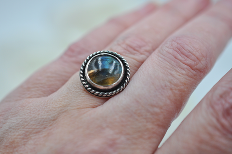 Silver ring with a gemstone on a person's finger against a neutral background
