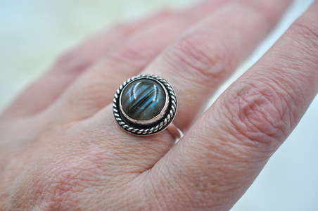 Silver ring with a stone on a person's finger against a blurred background
