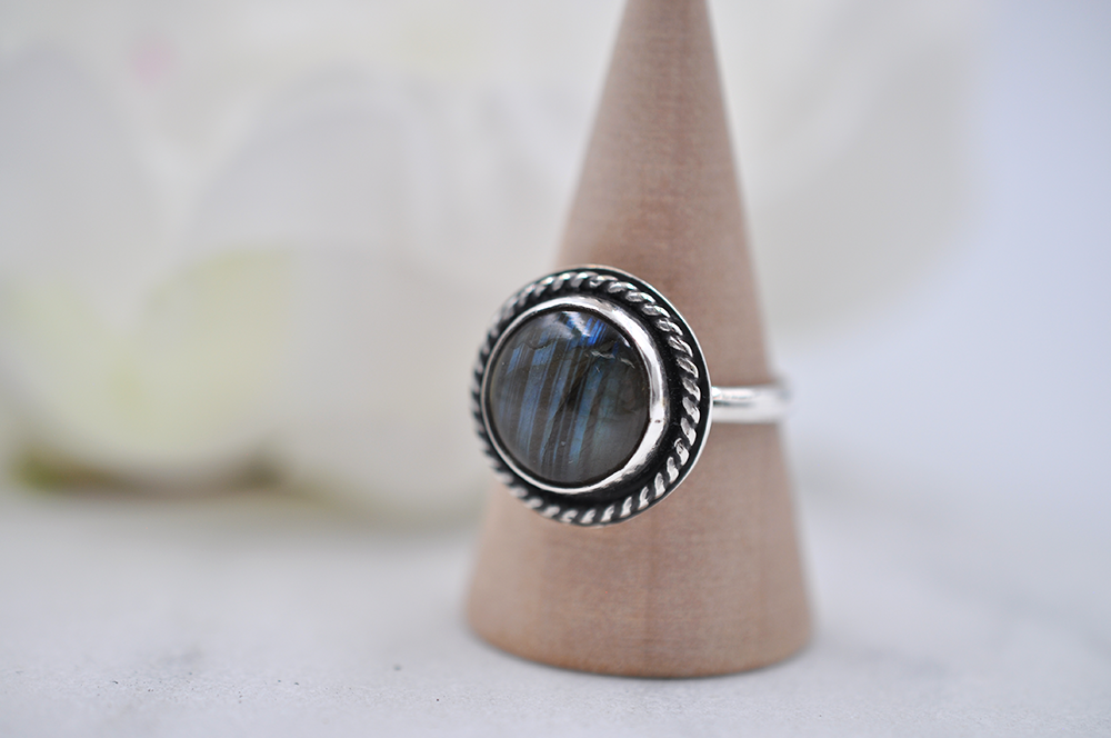 Silver ring with a dark stone on a wooden stand against a blurred background