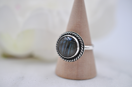 Silver ring with a dark stone on a wooden stand against a blurred background