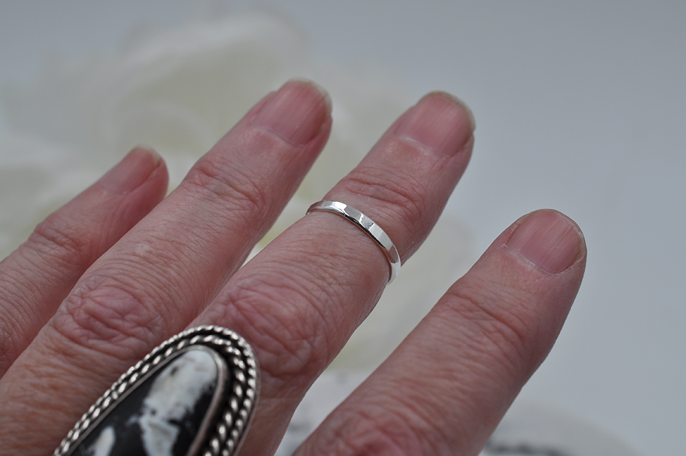 Close-up of a hand wearing a single silver midi ring on a blurred background