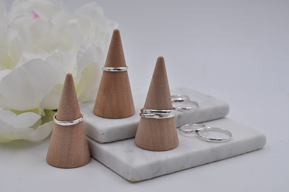 Wooden ring stands on a marble surface with silver hammered textured rings displayed.