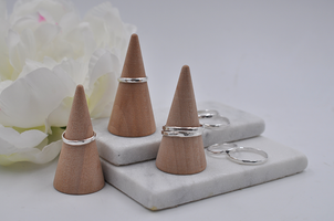 Wooden ring stands on a marble surface with silver hammered textured rings displayed.