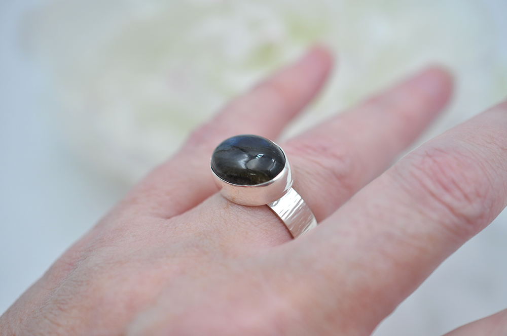 Silver ring with a dark blue stone on a hand against a blurred background