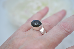 Silver ring with a dark blue stone on a hand against a blurred background