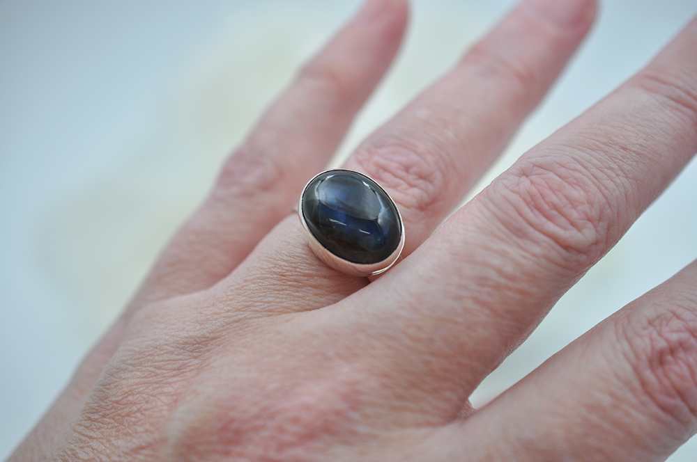 Hand wearing a ring with a dark blue stone on a light background