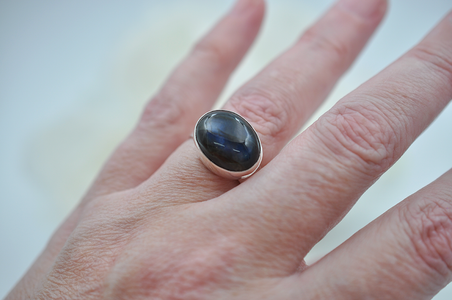 Hand wearing a ring with a dark blue stone on a light background