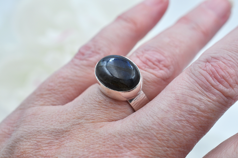 Silver ring with a dark blue stone on a person's finger against a neutral background