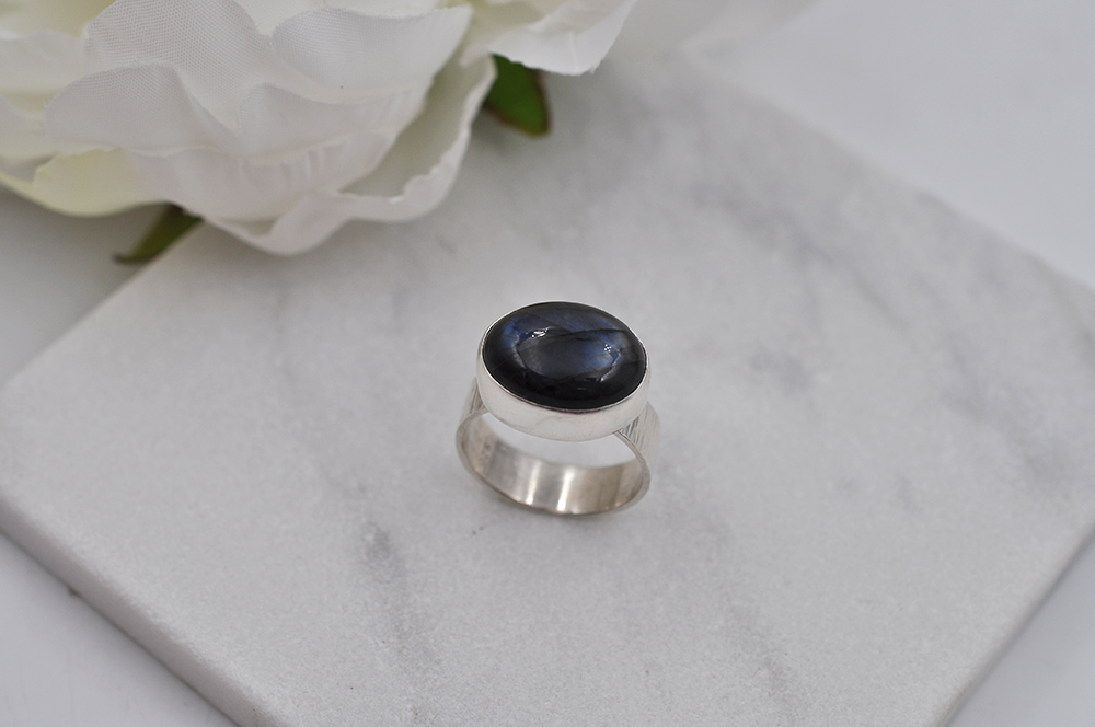 Silver ring with a dark stone on a marble surface with white flowers.
