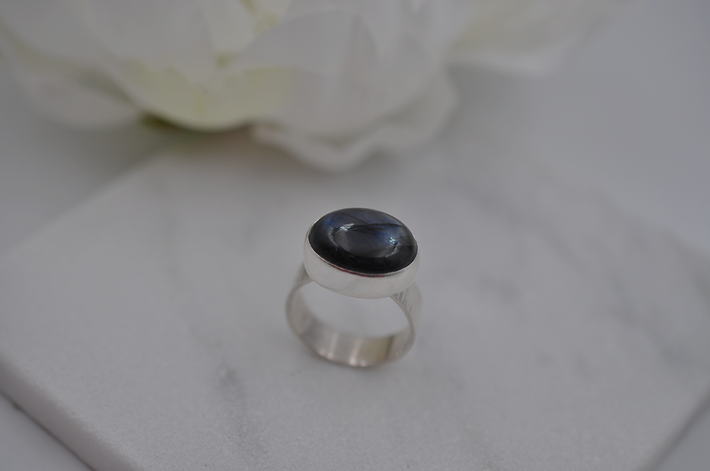 Silver ring with a dark blue stone on a marble surface with white flowers in the background