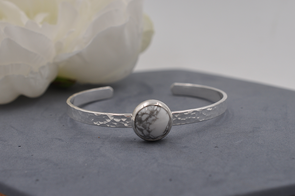 Silver hammered cuff bracelet with a round gray and white stone on a gray surface