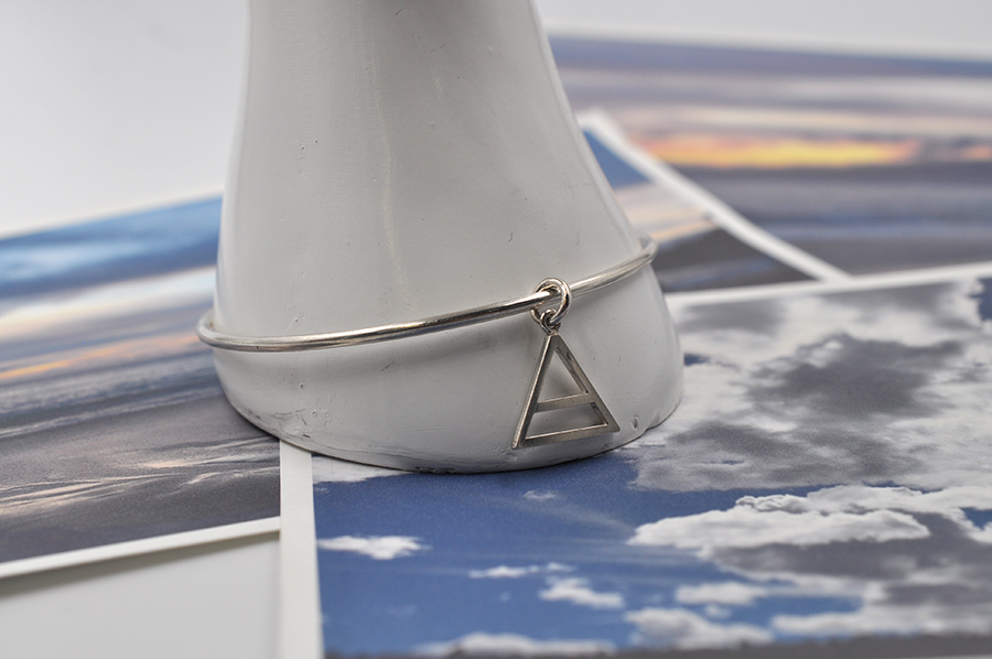 Pictured here is a round sterling silver bangle bracelet with a small air charm hanging from the continuous circle. Air symbol in a triangle with a line through the center. 