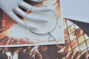 Round sterling silver continuous bangle braclet is showing laying on a mannequin hand's fingertips showcasing a dainty triangle indicative of the fire symbol.   