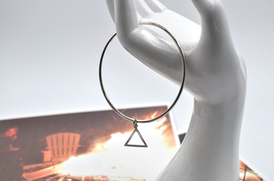 Round sterling silver continuous bangle bracelet is shown hanging from a white mannequin hand showcasing a dainty triangle charm that has shifted to the bottom of the round bracelet. This triangle charge is indicative of the fire symbol.