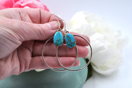 A pair of sterling silver hoop earrings with natural turquoise mountain turquoise stones, displayed against a floral background.