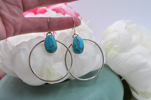 A pair of sterling silver hoop earrings with natural turquoise mountain turquoise stones, displayed against a floral background.