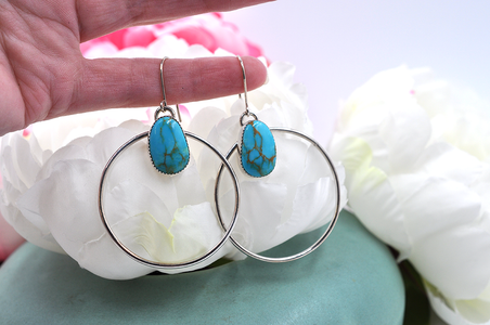 A pair of sterling silver hoop earrings with natural turquoise mountain turquoise stones, displayed against a floral background.