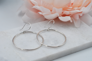 Round sterling silver drop hoop earrings pictured in an angled view laying flat on a marble slab. 