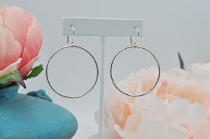 Sterling silver round drop hoop earrings hanging from an earring stand to show length. 