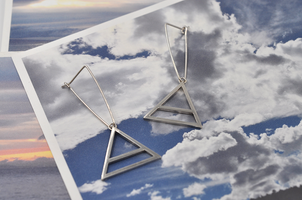 Featured here is a pair of sterling silver triangular drop hoops with a large air charm hanging from the bottom point of the triangle. The air symbol featured here is a triangle with a line through the center. 