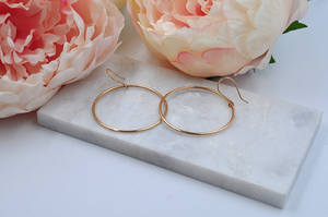 Large gold drop hoops laying flat pictured from a side angle.