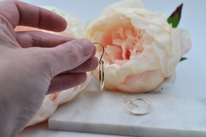 Side view of small gold drop hoop earrings pictured in model's hand for size. Drop hoop width is just shy of one inch. 