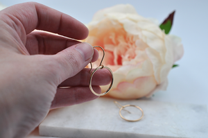 Angled view of small gold drop hoop pictured in model's hand for size. Drop hoop width is just shy of one inch. 