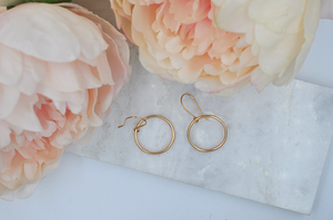 Gold round drop hoop earrings that measure approximately one inch in width pictured from above..
